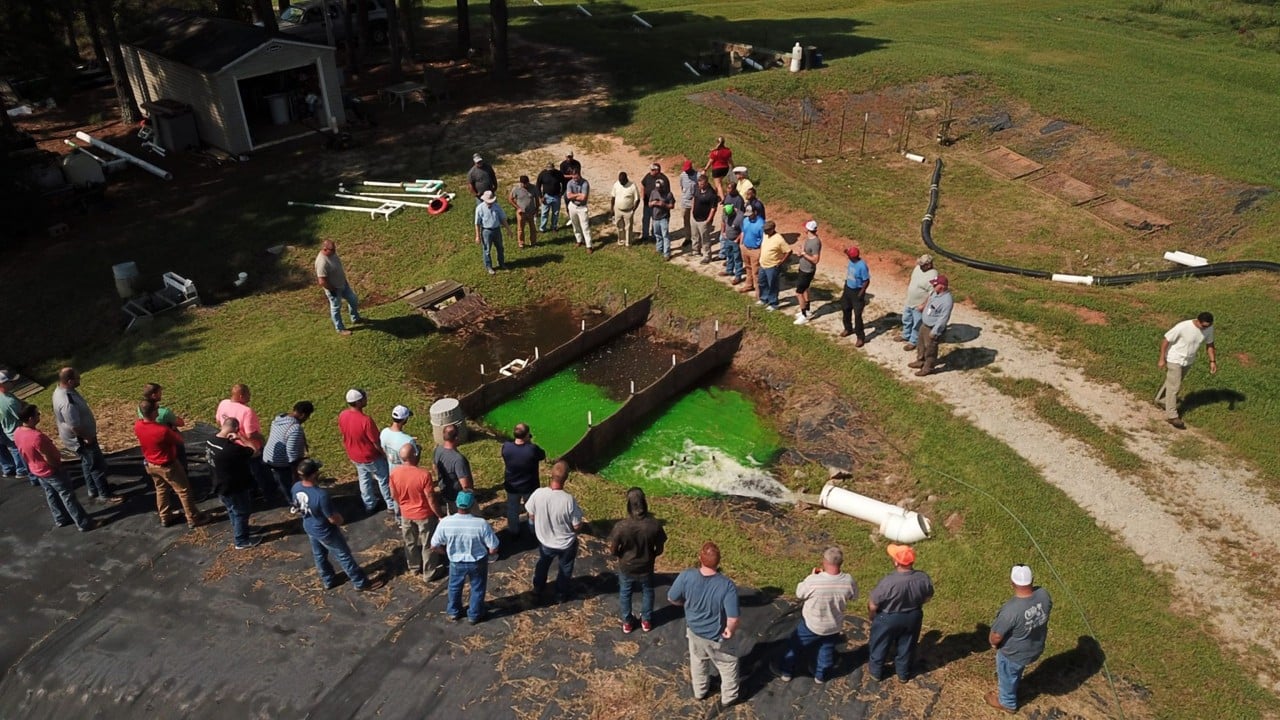 Demonstration of a skimmer basin with baffles. A pipe discharges turbulent water into a skimmer basin with baffles. Green dye shows how baffles dissipate energy and convert turbulent flow to plug flow.
